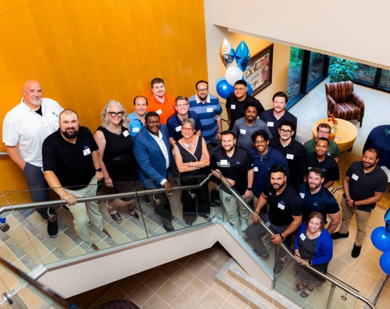 Group of diverse coworkers posing on a staircase in a bright atrium with balloons for a celebration.