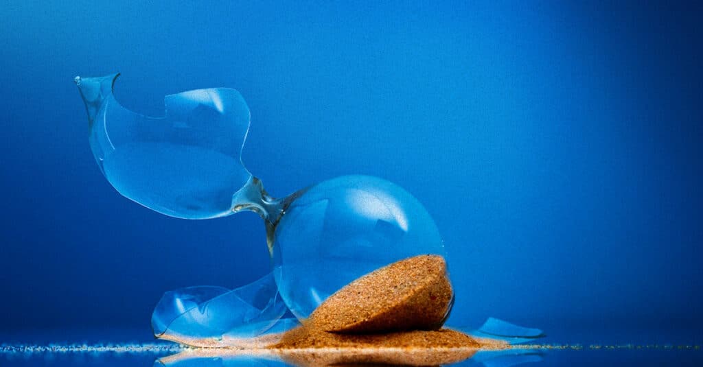 Blue glass ornament shattered into pieces with a small pile of sand on a blue background